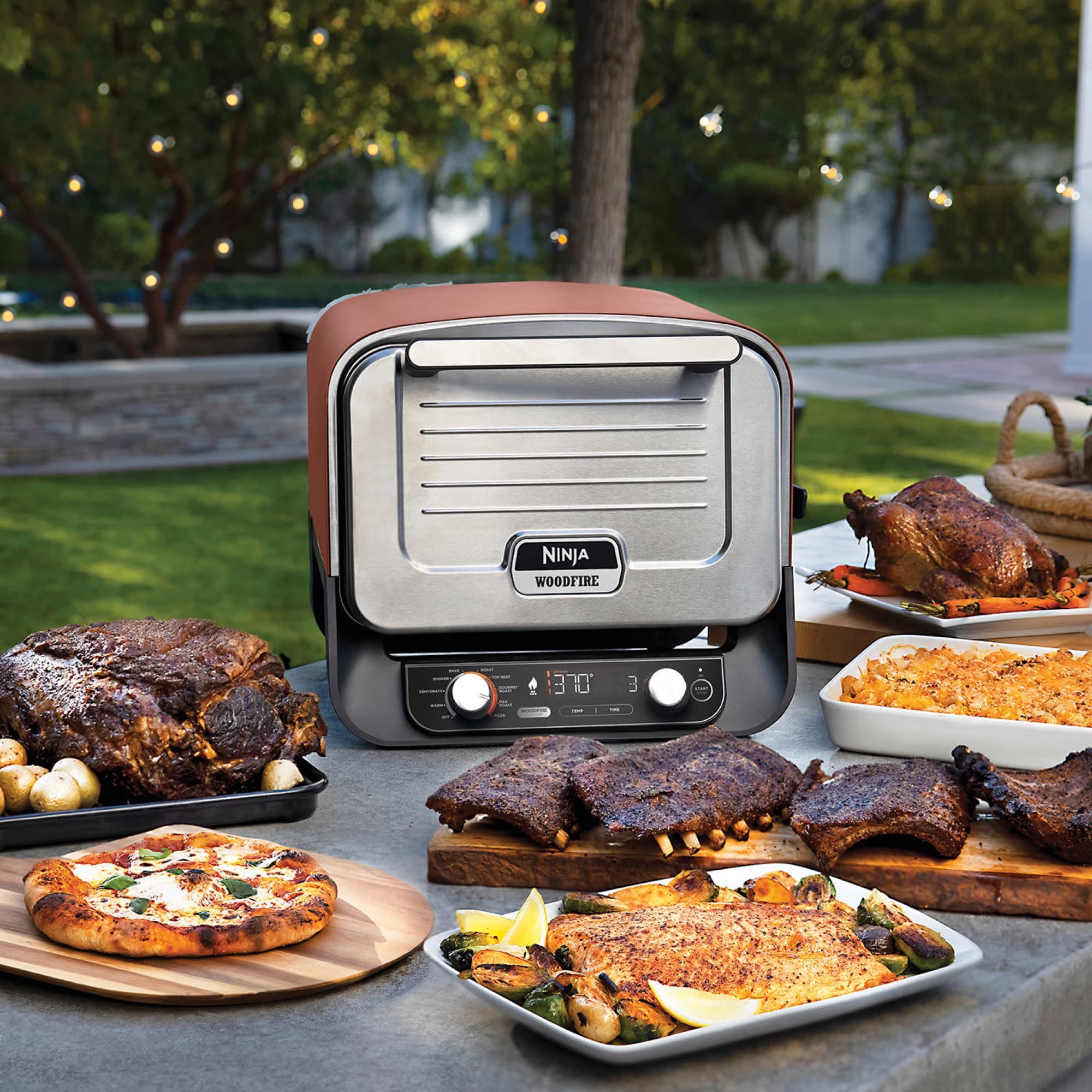 The oven on an outdoor table with pizza, ribs and roast