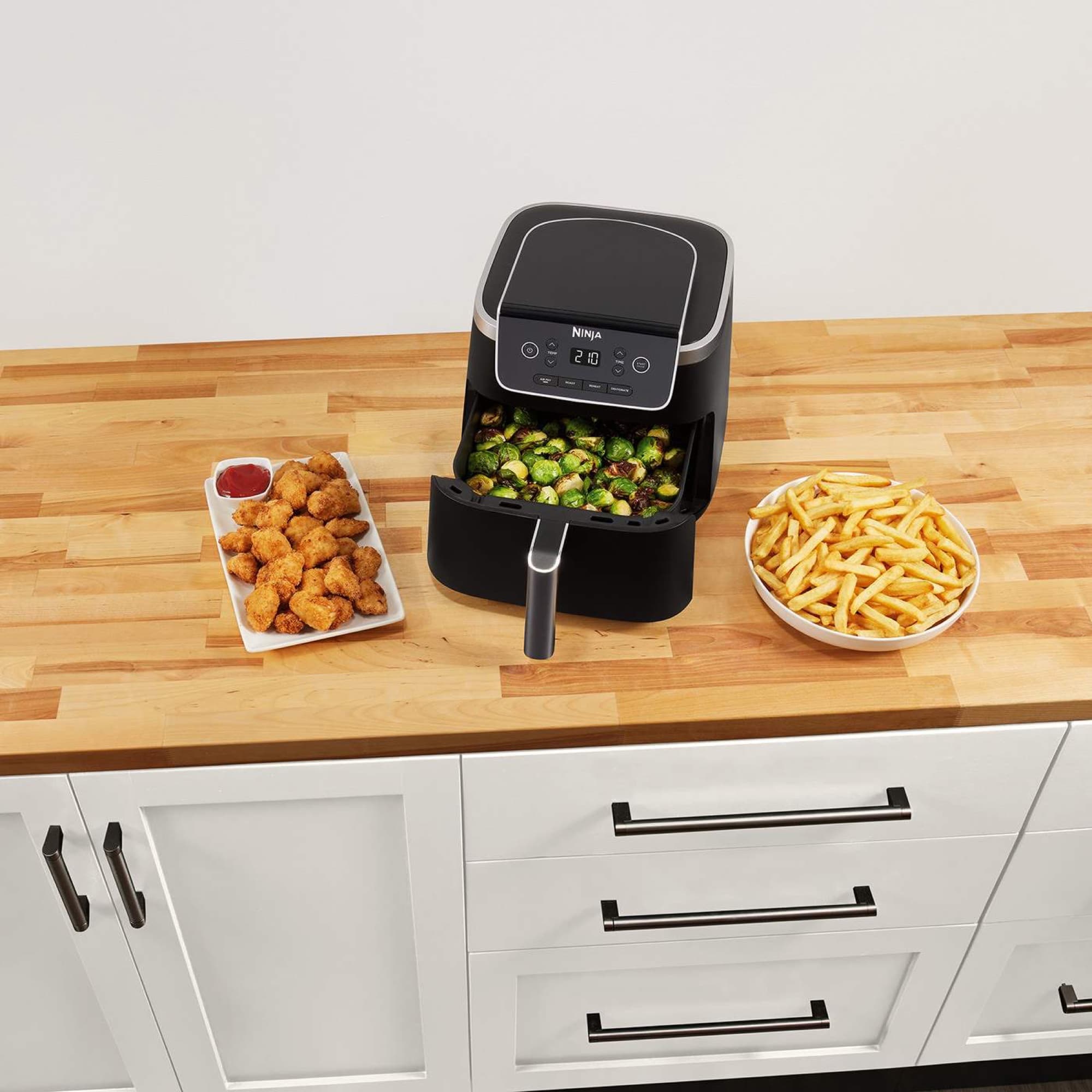 The air fryer on the worktop with Brussels sprouts in the drawer, chicken and fries beside it