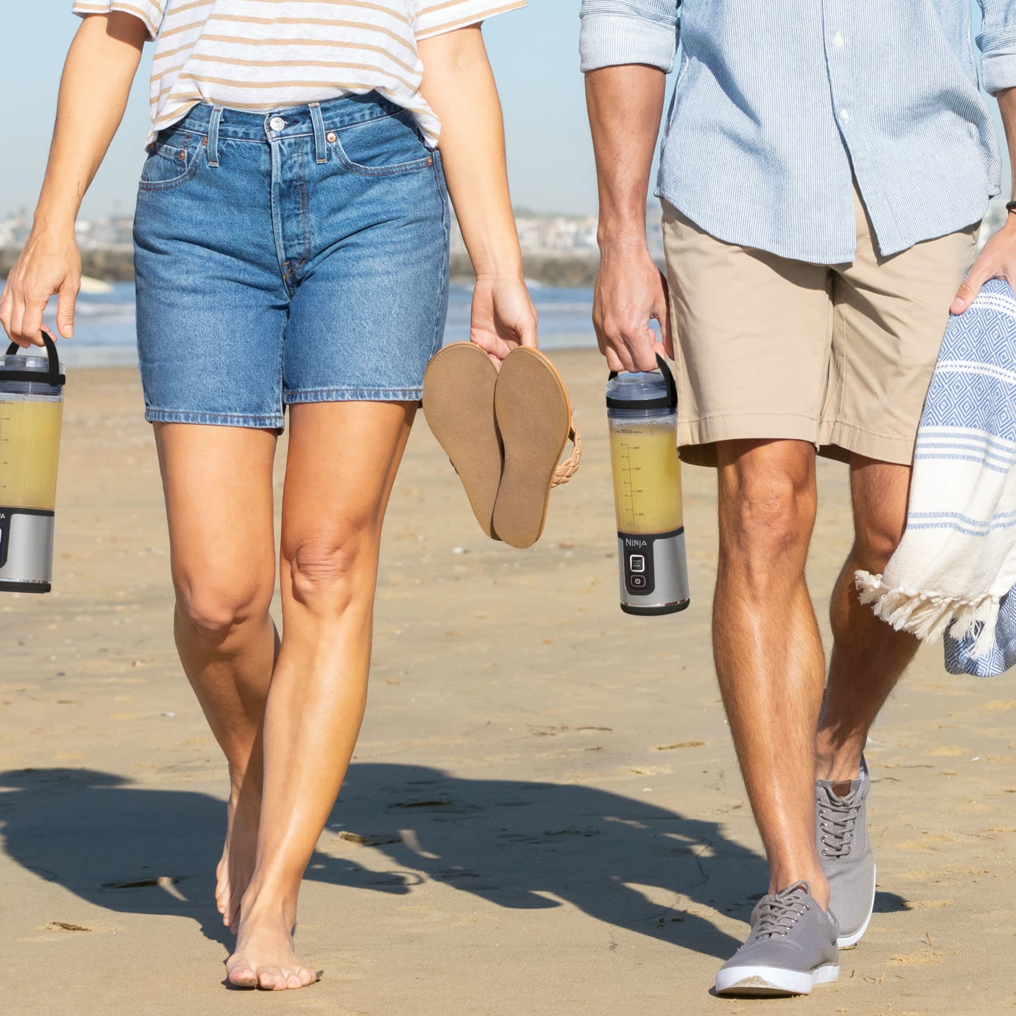 Two people carrying a blender each on the beach